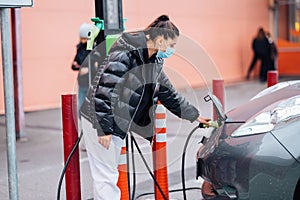 Young beautiful woman traveling by electric car having stop at charging station