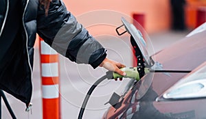 Young beautiful woman traveling by electric car having stop at charging station