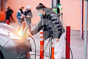 Young beautiful woman traveling by electric car having stop at charging station