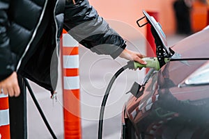 Young beautiful woman traveling by electric car having stop at charging station