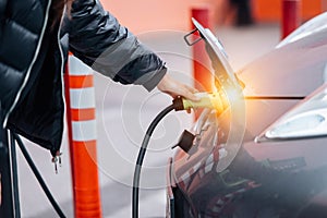 Young beautiful woman traveling by electric car having stop at charging station