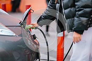 Young beautiful woman traveling by electric car having stop at charging station