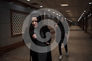 A young beautiful woman tries to escape from a robber in black clothes . in the underpass. at night