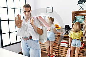 Young beautiful woman with two daughters holding shopping bags at retail shop with open hand doing stop sign with serious and