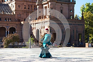 Young and beautiful woman with typical green dress with ruffles and dancing flamenco in plaza de espana in seville, andalusia,
