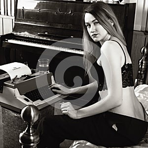 Young beautiful woman typing on a retro typewriter. female writer in bra and men`s trousers. black and white