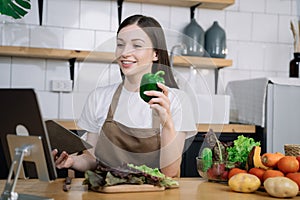 Young beautiful woman using laptop computer searching and learning for cooking healthy food from fresh vegetables and fruits in