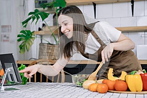 Young beautiful woman using laptop computer searching and learning for cooking healthy food from fresh vegetables and fruits in