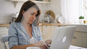 Young beautiful woman is using laptop sitting at table in kitchen at home.