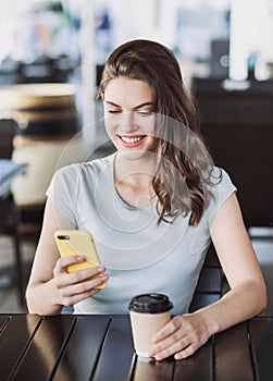 Young beautiful woman using smart phone in a cafe. Pretty student girl sitting in a coffee shop and typing on mobile phone