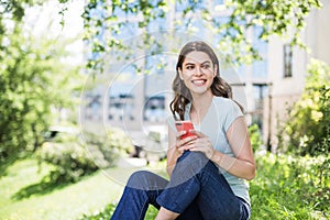 Young beautiful woman using smart phone in a city park. Smiling girl resting outdoor. Student lifestyle concept