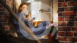 Young Beautiful Woman Using Smartphone and Enjoying her Morning Coffee While Sitting on her Bedroom