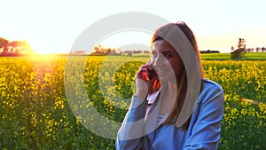 Young beautiful woman using smartphone on the silhouette of the sunset field.