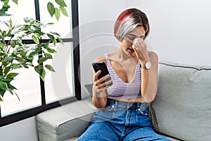 Young beautiful woman using smartphone typing message sitting on the sofa tired rubbing nose and eyes feeling fatigue and headache