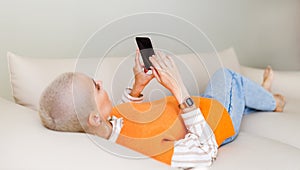 Young beautiful woman with very short hair   relaxing at home with smartphone, surfing internet