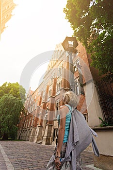 Young beautiful woman walking down the street along an old brick building against the background of sunlight