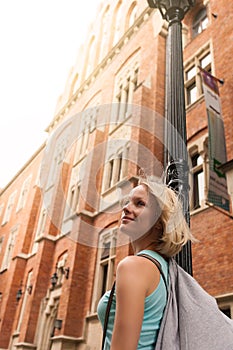 Young beautiful woman walking down the street along an old brick building against the background of sunlight