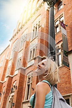 Young beautiful woman walking down the street along an old brick building against the background of sunlight