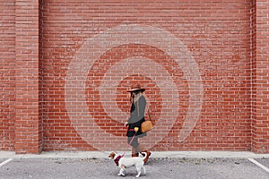 Young beautiful woman walking with her dog by the street. Orange brick wall background. Love and pets outdoors