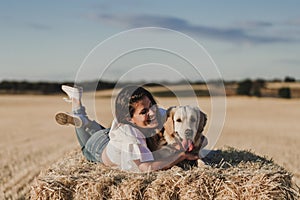 Young beautiful woman walking with her golden retriever dog on a yellow field at sunset. Nature and lifestyle outdoors