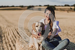 Young beautiful woman walking with her golden retriever dog on a yellow field at sunset. Nature and lifestyle outdoors