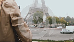 Young beautiful woman walking in Paris, France and taking photos of Eiffel tower in fog on smartphone or mobile phone.