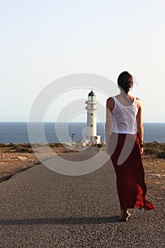 Young beautiful woman walking slowly to Cap de Barberias lighthouse during an amazing summer sunset