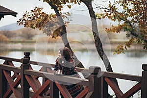 Young beautiful woman in a warm classic coat drinking tea near lake