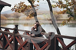 Young beautiful woman in a warm classic coat drinking tea near lake