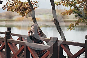 Young beautiful woman in a warm classic coat drinking tea near lake