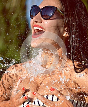 Young beautiful woman with water splashes in sunglasses and bikini laughing smiling