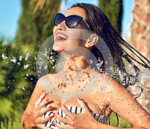 Young beautiful woman with water splashes in sunglasses and bikini laughing smiling