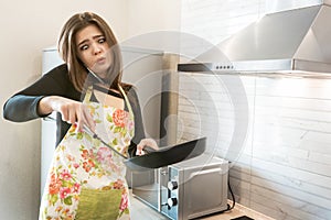 Young beautiful woman wearing apron cooking in the kitchen while having phone conversation looks astonished everyday routine