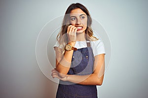 Young beautiful woman wearing apron over grey  background looking stressed and nervous with hands on mouth biting nails