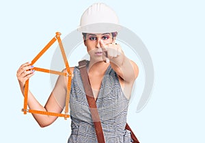 Young beautiful woman wearing architect hardhat holding build project pointing with finger to the camera and to you, confident