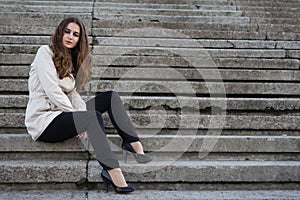 Young beautiful woman wearing beige jacket sitting on concrete s