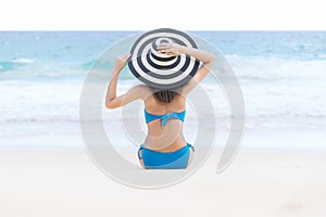 Young beautiful woman wearing bikini and relaxing on the white sandy beach near the waves of blue on tropical beach