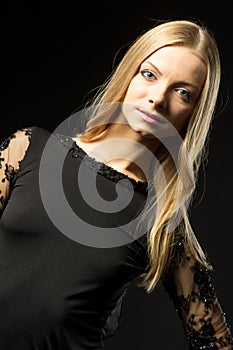 Young beautiful woman wearing black evening dress with naked shoulders posing over black background