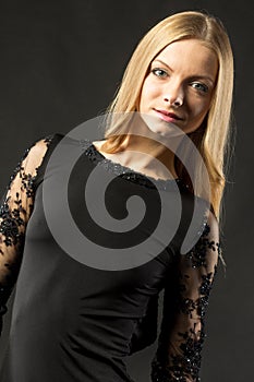 Young beautiful woman wearing black evening dress with naked shoulders posing over black background