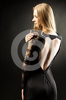 Young beautiful woman wearing black evening dress with naked shoulders posing over black background