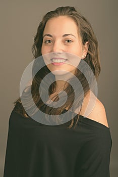 Young beautiful woman wearing black off-shoulder top against gray background