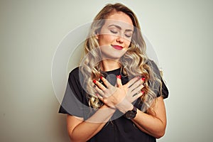 Young beautiful woman wearing black t-shirt standing over white isolated background smiling with hands on chest with closed eyes