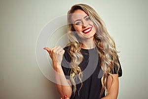 Young beautiful woman wearing black t-shirt standing over white isolated background smiling with happy face looking and pointing