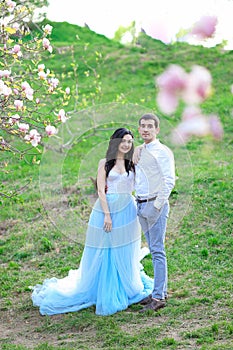 Young beautiful woman wearing blue dress and walking near magnolia with boyfriend.