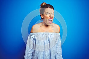 Young beautiful woman wearing bun hairstyle over blue isolated background angry and mad screaming frustrated and furious, shouting