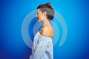 Young beautiful woman wearing bun hairstyle over blue isolated background looking to side, relax profile pose with natural face