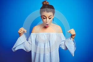 Young beautiful woman wearing bun hairstyle over blue isolated background Pointing down with fingers showing advertisement,