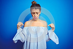 Young beautiful woman wearing bun hairstyle over blue isolated background Pointing down looking sad and upset, indicating