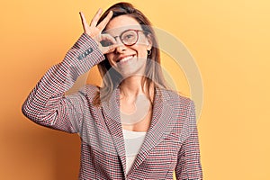 Young beautiful woman wearing business clothes and glasses smiling happy doing ok sign with hand on eye looking through fingers