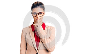 Young beautiful woman wearing business shirt and glasses asking to be quiet with finger on lips